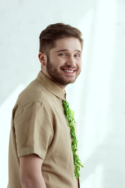 Vista lateral del joven hombre sonriente con corbata hecha de rúcula, concepto de estilo de vida vegano - foto de stock