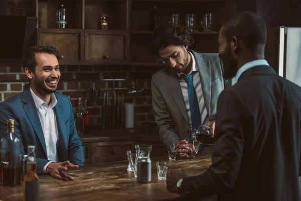 Male friends in suits smiling each other, talking and drinking alcoholic beverages during stag party — Stock Photo