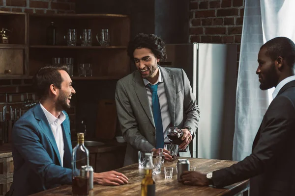 Alegre jóvenes amigos masculinos beber bebidas alcohólicas y hablar mientras festejan juntos - foto de stock