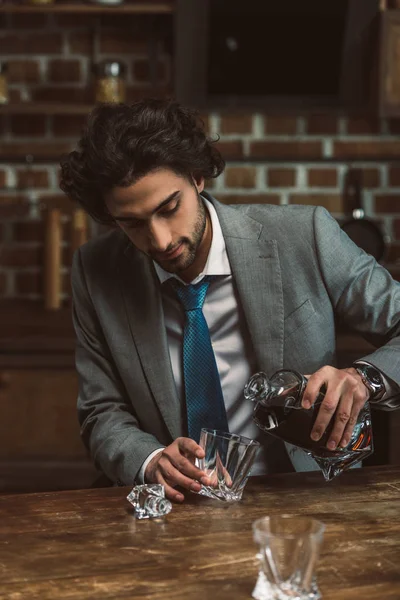 Hombre joven en traje vertiendo whisky en vidrio - foto de stock