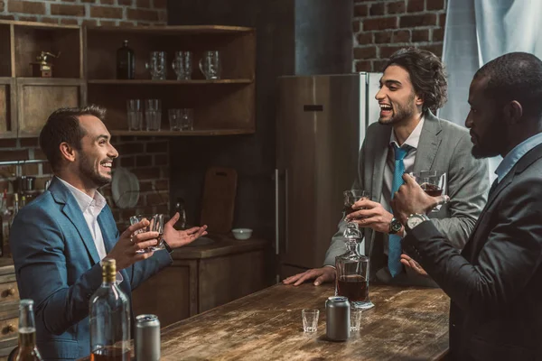 Joyeux jeunes hommes multiethniques parlant et buvant du whisky ensemble — Photo de stock