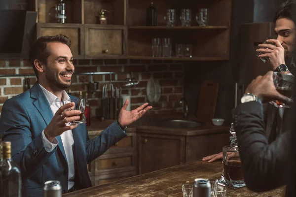 Обрезанный снимок молодых людей в костюмах, пьющих виски и разговаривающих друг с другом — стоковое фото