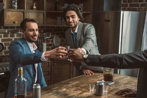 Cropped shot of happy male friends clinking glasses of whisky while partying together — Stock Photo