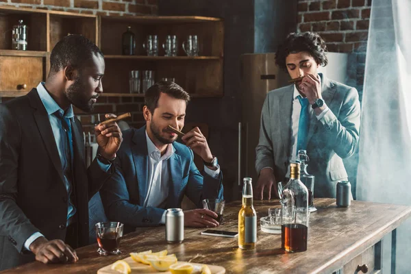 Beaux jeunes hommes multiethniques en costumes tenant des cigares tout en faisant la fête ensemble — Photo de stock