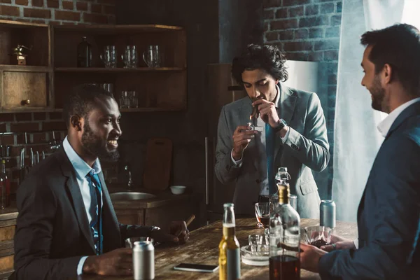 Lächelnde junge männliche Freunde in offizieller Kleidung rauchen Zigarren und trinken alkoholische Getränke, während sie zusammen feiern — Stockfoto