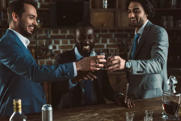 Joyeux jeunes amis masculins en costumes cliquetis verres de whisky — Photo de stock