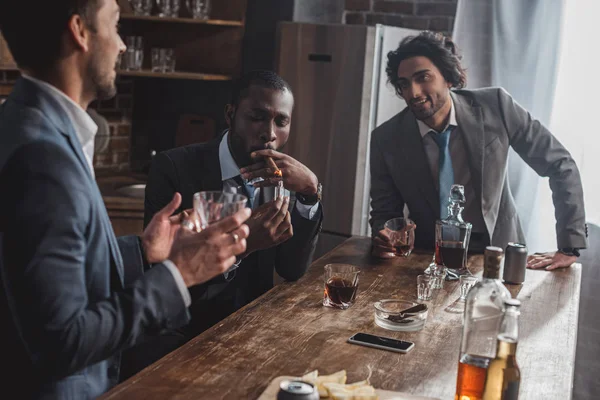 Cropped shot of smiling multiethnic businessmen talking while smoking cigars and drinking whiskey — Stock Photo