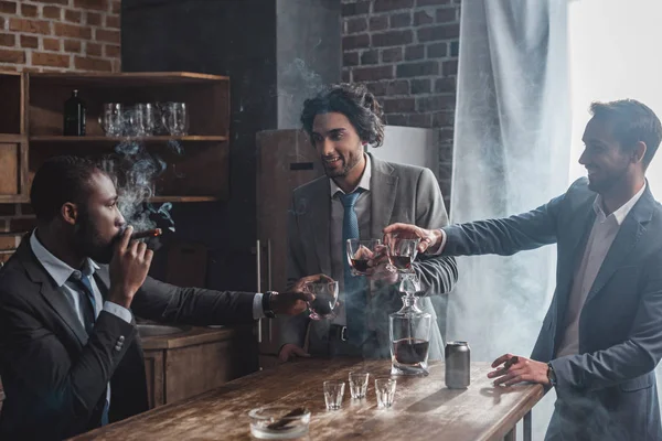 Fröhliche männliche Freunde in feierlicher Kleidung rauchen Zigarren und klirren Whiskey-Gläser — Stockfoto