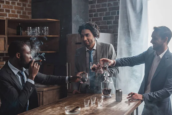 Alegre macho amigos en formal desgaste fumar cigarros y tintineo vasos de whisky - foto de stock