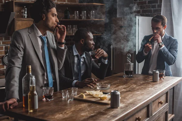 Молоді багатонаціональні бізнесмени курять сигари і п'ють алкоголь, беручи участь разом — стокове фото