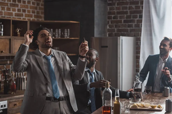 Jóvenes empresarios entusiasmados fumando cigarros y bebiendo bebidas alcohólicas juntos - foto de stock