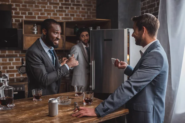 Smiling multiethnic businessmen looking at each other and friend hiding behind refrigerator while partying together — Stock Photo