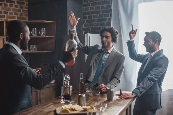 Excitados empresarios multiétnicos fumando cigarros y bebiendo whisky - foto de stock