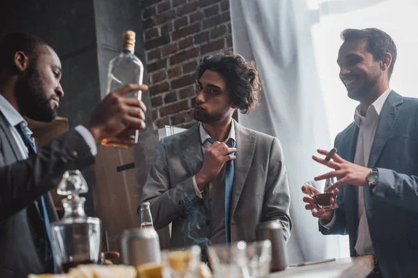 Vista de bajo ángulo de jóvenes empresarios multiétnicos fumando cigarros y bebiendo whisky - foto de stock