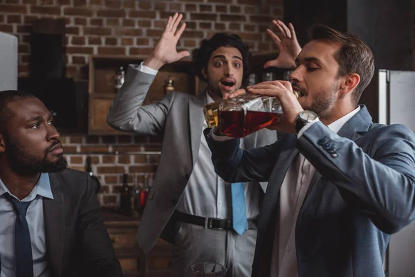 Мультиэтнические бизнесмены смотрят на друга, пьющего алкогольные напитки из бутылок — стоковое фото