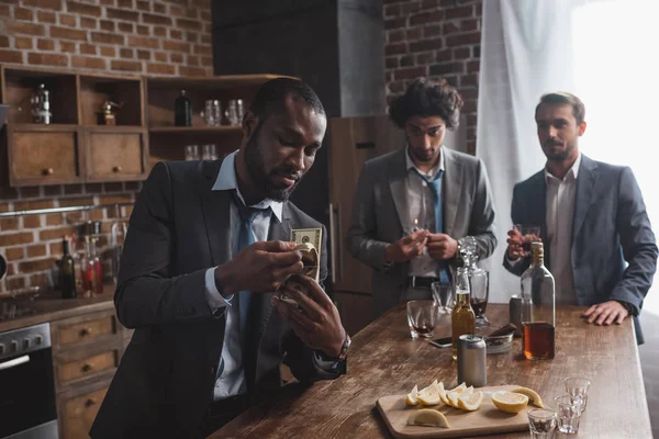 African american businessman counting dollar banknotes while drinking alcohol with friends — Stock Photo