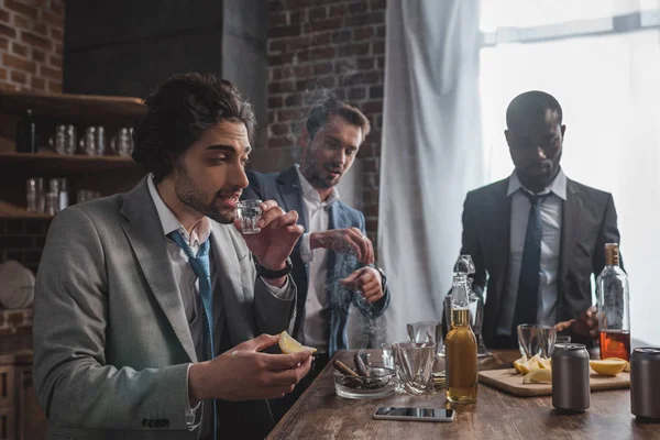 Amigos masculinos multiétnicos en desgaste formal beber tequila y fumar cigarros - foto de stock