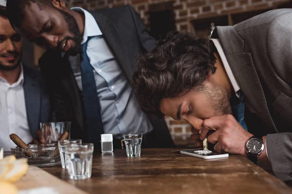 Cropped shot of multiethnic businessmen looking at friend taking cocaine — Stock Photo