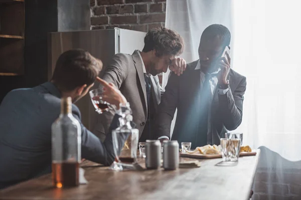 Hombres multiétnicos en trajes que beben alcohol y hablan por teléfono inteligente - foto de stock