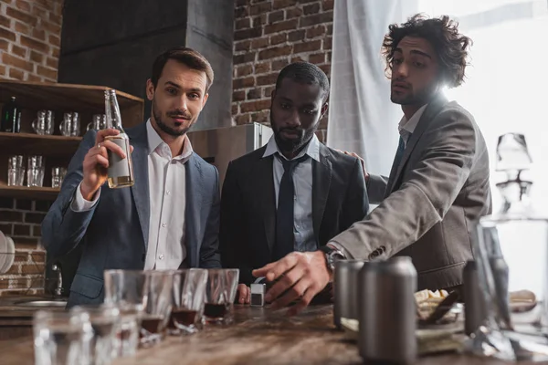 Jóvenes amigos multiétnicos en trajes que beben bebidas alcohólicas juntos - foto de stock
