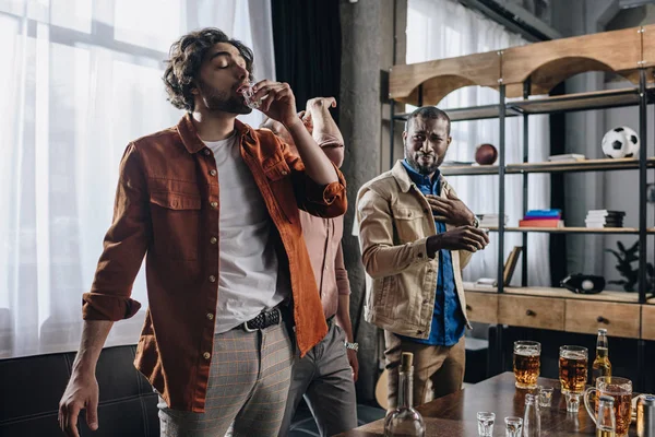 Jovem multiétnico masculino amigos bebendo tequila enquanto festejando juntos dentro de casa — Fotografia de Stock