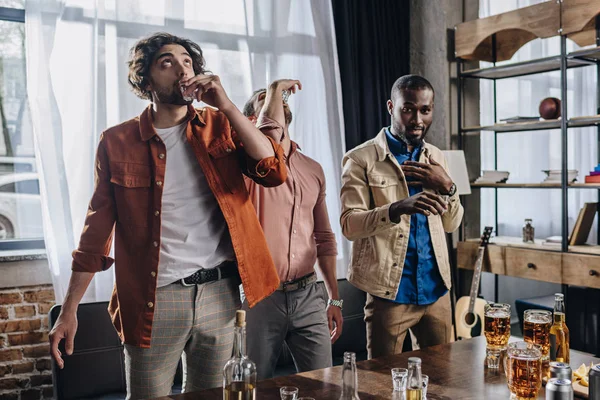 Multiethnische männliche Freunde trinken Tequila, während sie drinnen zusammen feiern — Stockfoto