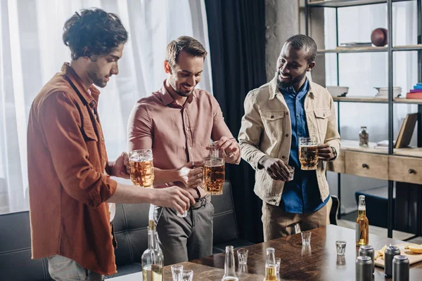 Sonrientes amigos masculinos multiétnicos bebiendo bebidas alcohólicas y festejando juntos - foto de stock