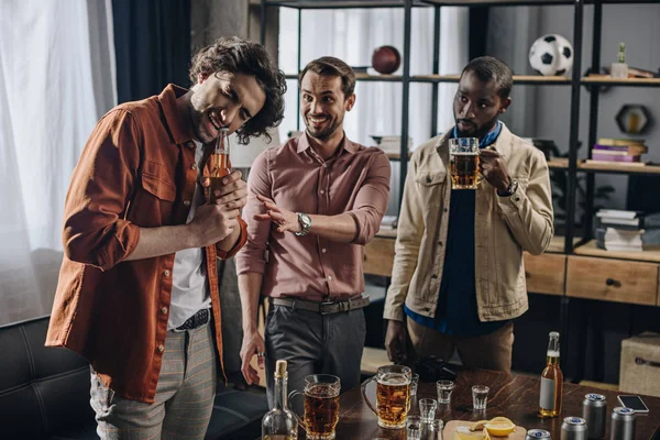 Junge multiethnische Männer schauen Freund beim Öffnen einer Bierflasche mit Zähnen an — Stockfoto