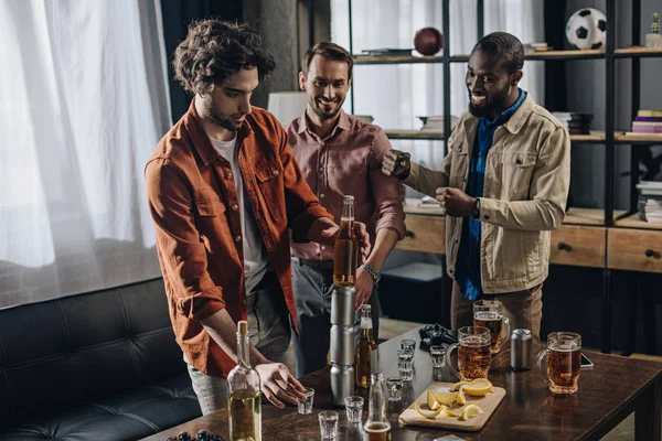 Amigos multiétnicos sonrientes construyendo torre de botella de cerveza y latas mientras festejan juntos - foto de stock