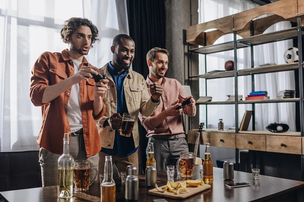 Lächelnde multiethnische Männer, die mit Joysticks spielen und gemeinsam feiern — Stockfoto