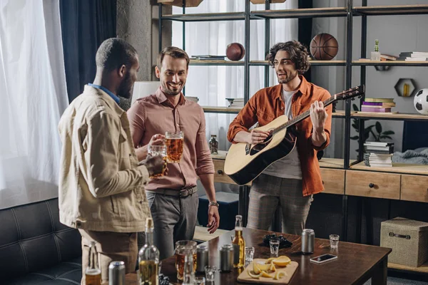 Fröhliche multiethnische männliche Freunde, die zusammen Bier trinken und Gitarre spielen — Stockfoto