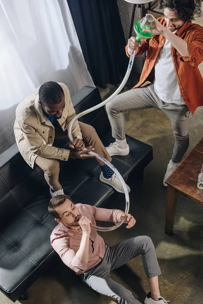 High angle view of smiling multiethnic friends drinking beer from beer bong — Stock Photo