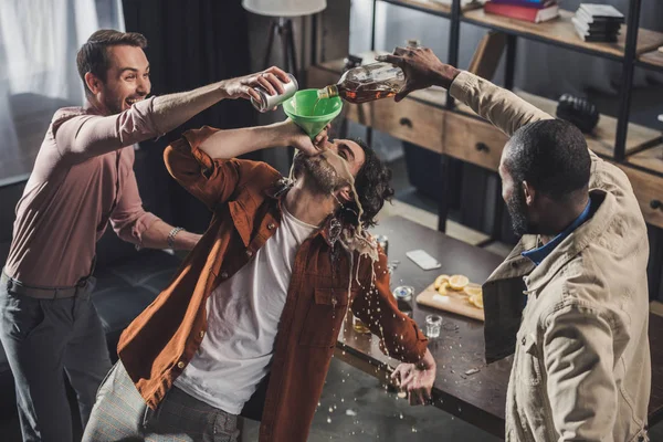 Vista de ángulo alto del hombre bebiendo del embudo mientras sus amigos vierten bebidas alcohólicas - foto de stock