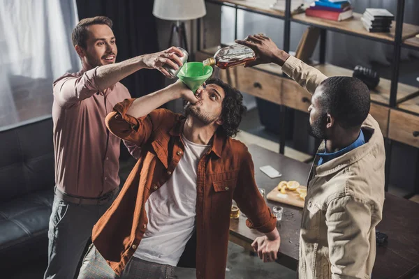 Vue grand angle de l'homme buvant de l'entonnoir tandis que les amis versant des boissons alcoolisées de la bouteille en verre et peut — Photo de stock