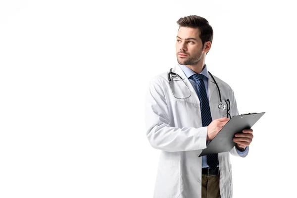 Nachdenklicher männlicher medizinischer Mitarbeiter in weißem Mantel mit Stethoskop und Schrift im Klemmbrett isoliert auf weiß — Stockfoto