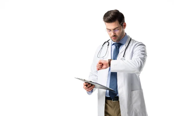 Doctor with clipboard wearing white coat with stethoscope and checking his watch isolated on white — Stock Photo