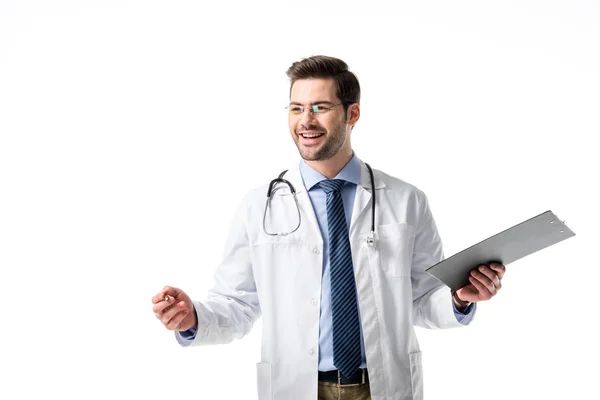 Alegre médico vistiendo abrigo blanco con estetoscopio y sujetando el portapapeles aislado en blanco - foto de stock