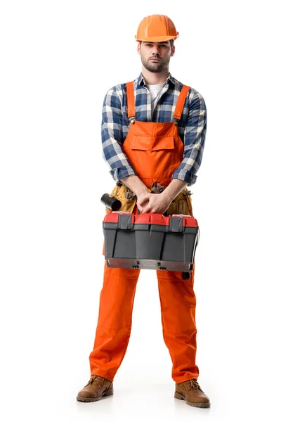 Confident handyman in orange overall and hard hat holding tool box isolated on white — Stock Photo