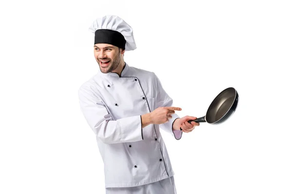 Chef sonriente en uniforme apuntando a la sartén en mano aislado en blanco — Stock Photo