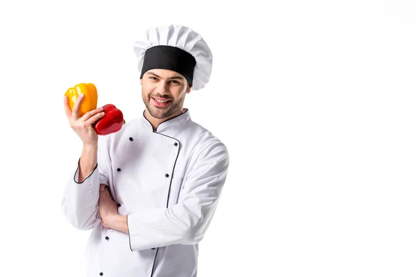 Усміхнений шеф-кухар в уніформі зі свіжим болгарським перцем в руці ізольовано на білому — стокове фото
