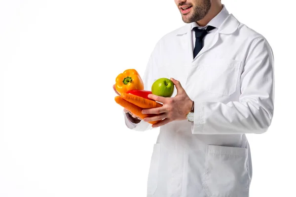 Abgeschnittene Aufnahme eines Ernährungswissenschaftlers im weißen Mantel mit frischem Gemüse und Apfel in den Händen isoliert auf weiß — Stockfoto