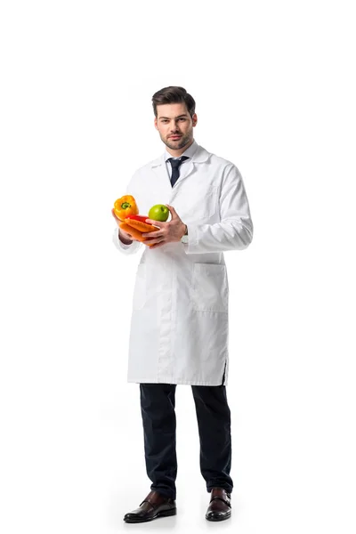 Nutritionist in white coat with fresh vegetables and apple in hands isolated on white — Stock Photo