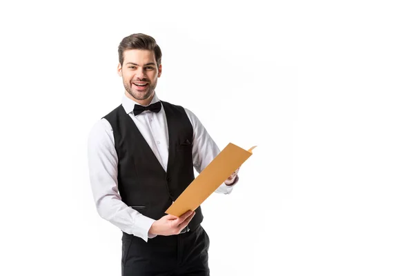 Портрет улыбающегося официанта в костюме жилета с меню, изолированным на белом — стоковое фото