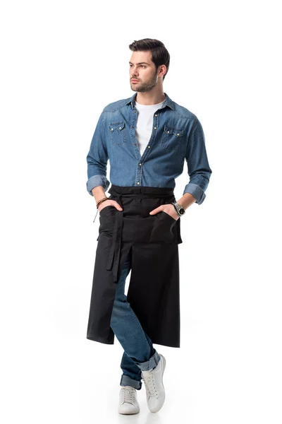 Young waiter in apron with hands in pockets looking away isolated on white — Stock Photo