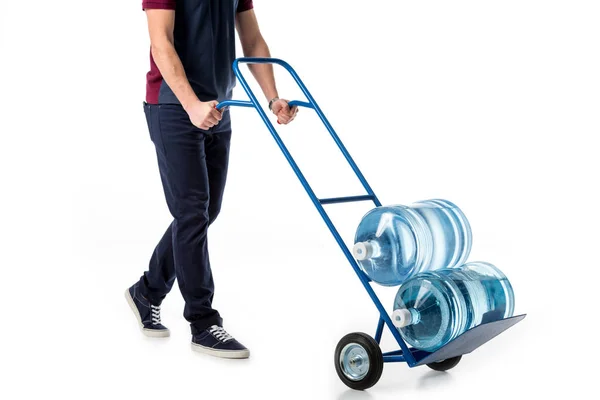 Partial view of delivery man in uniform pushing hand truck with large bottles of water isolated on white — Stock Photo