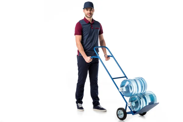 Livreur en uniforme poussant camion à main avec de grandes bouteilles d'eau isolé sur blanc — Photo de stock