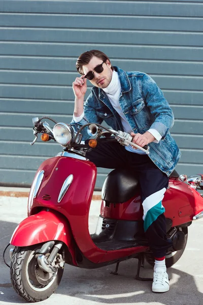 Beau jeune homme sur scooter rouge vintage regardant la caméra — Photo de stock