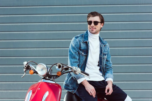 Heureux jeune homme en jean veste sur scooter rouge vintage — Photo de stock