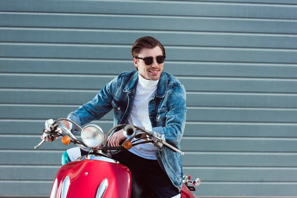 Glücklicher junger Mann in Jeansjacke auf rotem Oldtimer-Roller schaut weg — Stockfoto