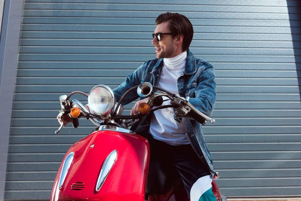 Jovem elegante em jaqueta de ganga na scooter vermelho vintage olhando para longe — Fotografia de Stock